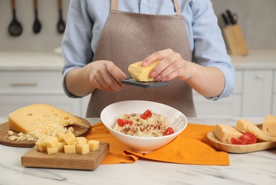 Photo of Woman grating cheese onto delicious pasta at white marble table in kitchen, closeup
