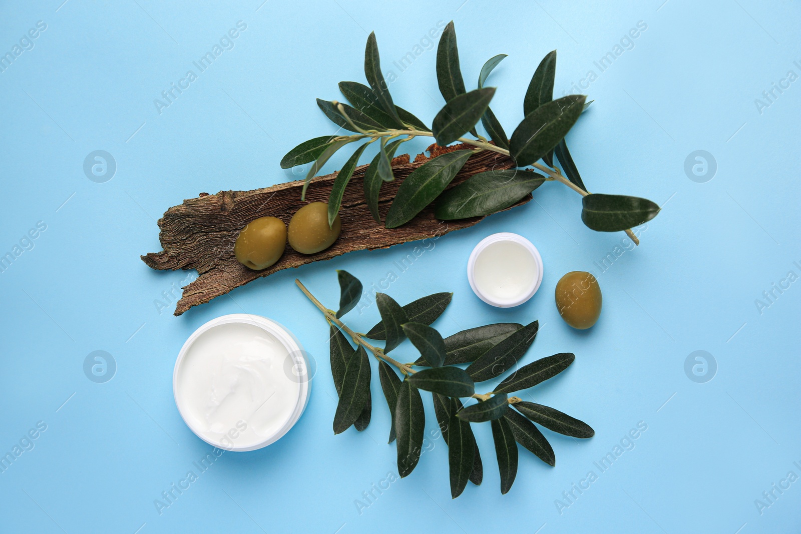 Photo of Flat lay composition with jars of cream and olives on light blue background