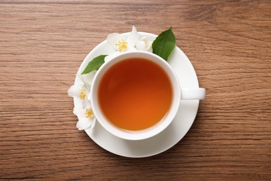 Photo of Cup of aromatic jasmine tea and fresh flowers on wooden table, top view