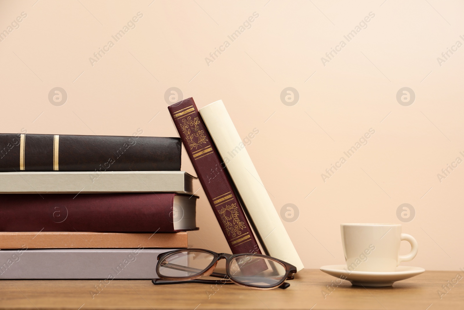 Photo of Books, glasses and cup of drink on wooden table near beige wall, space for text