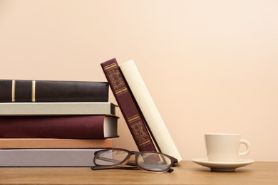 Books, glasses and cup of drink on wooden table near beige wall, space for text