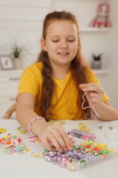 Cute girl making beaded jewelry at table in room, focus on hand