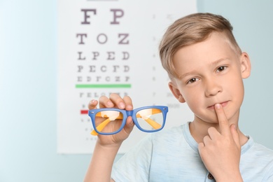 Photo of Cute little boy with eyeglasses in ophthalmologist office