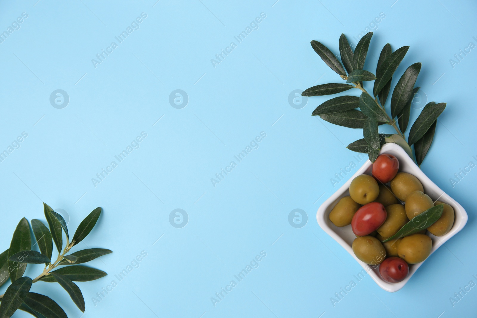 Photo of Different fresh olives and green leaves on light blue background, flat lay. Space for text