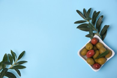 Photo of Different fresh olives and green leaves on light blue background, flat lay. Space for text