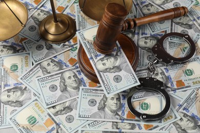 Photo of Judge's gavel, handcuffs and scales of justice on dollar banknotes, closeup