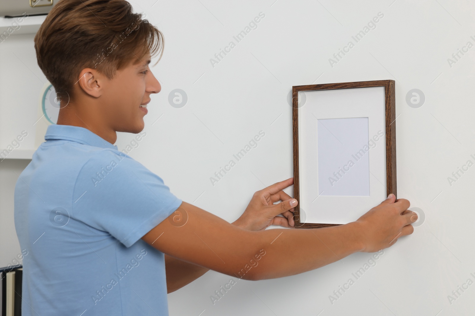 Photo of Young man hanging picture frame on white wall indoors