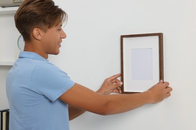 Photo of Young man hanging picture frame on white wall indoors