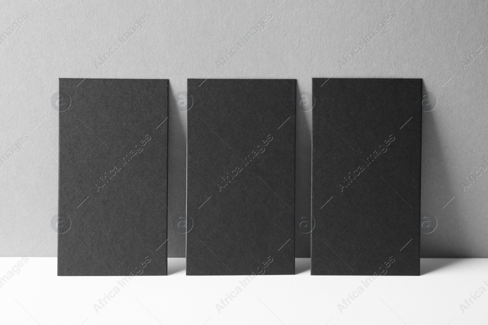 Photo of Blank black business cards on white table against grey background. Mockup for design