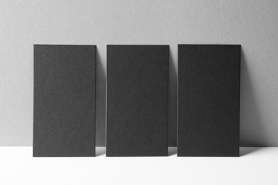 Photo of Blank black business cards on white table against grey background. Mockup for design