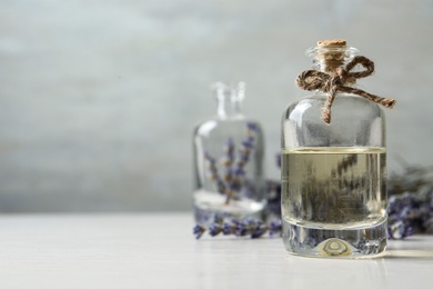 Photo of Bottle of natural essential oil and lavender flowers on white wooden table. Space for text