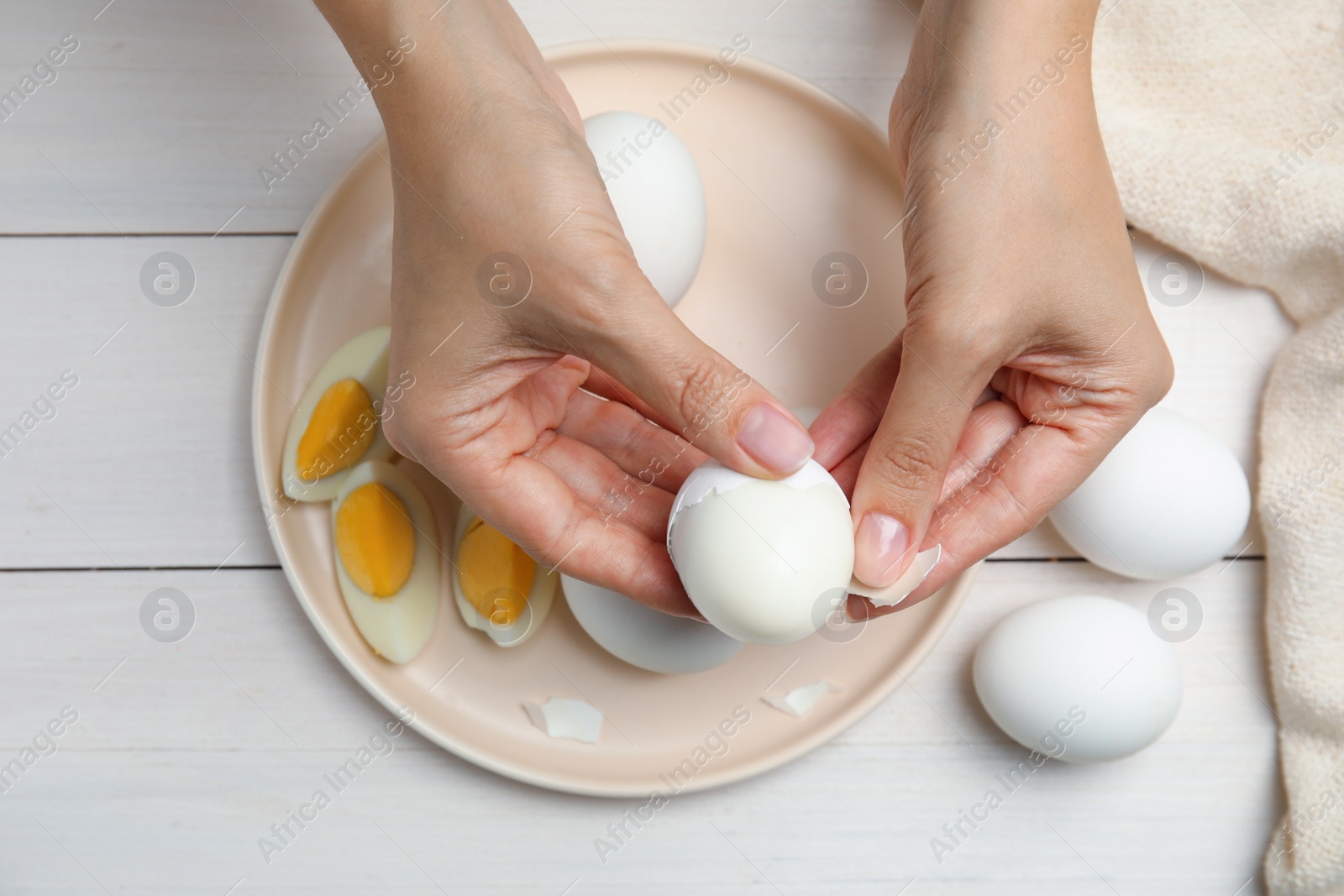 Photo of Woman peeling boiled egg at white wooden table, top view