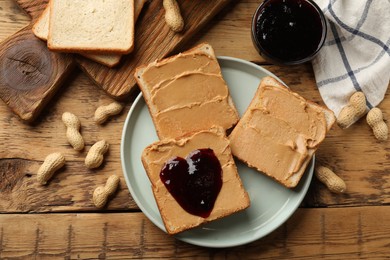 Photo of Tasty peanut butter sandwiches with jam and peanuts on wooden table, flat lay