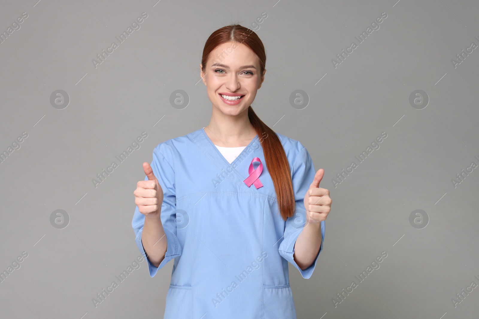 Photo of Mammologist with pink ribbon showing thumbs up on gray background. Breast cancer awareness