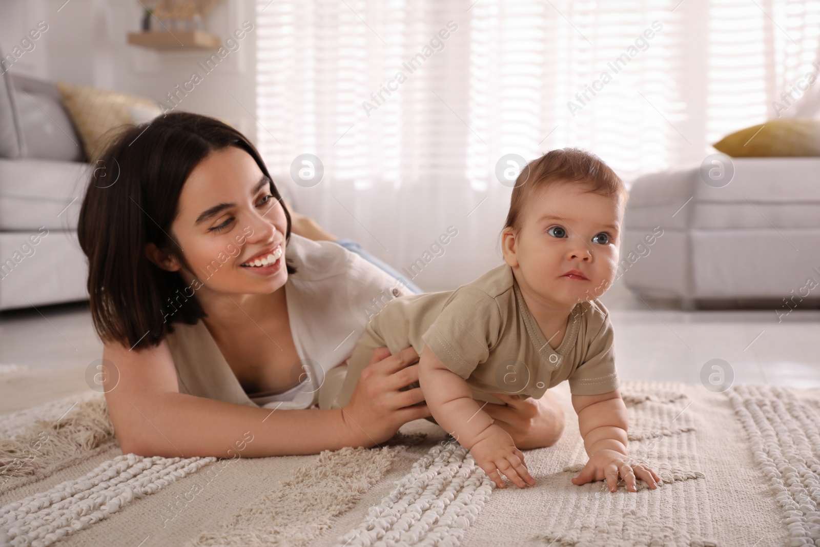 Photo of Happy young mother helping her cute baby to crawl on floor at home