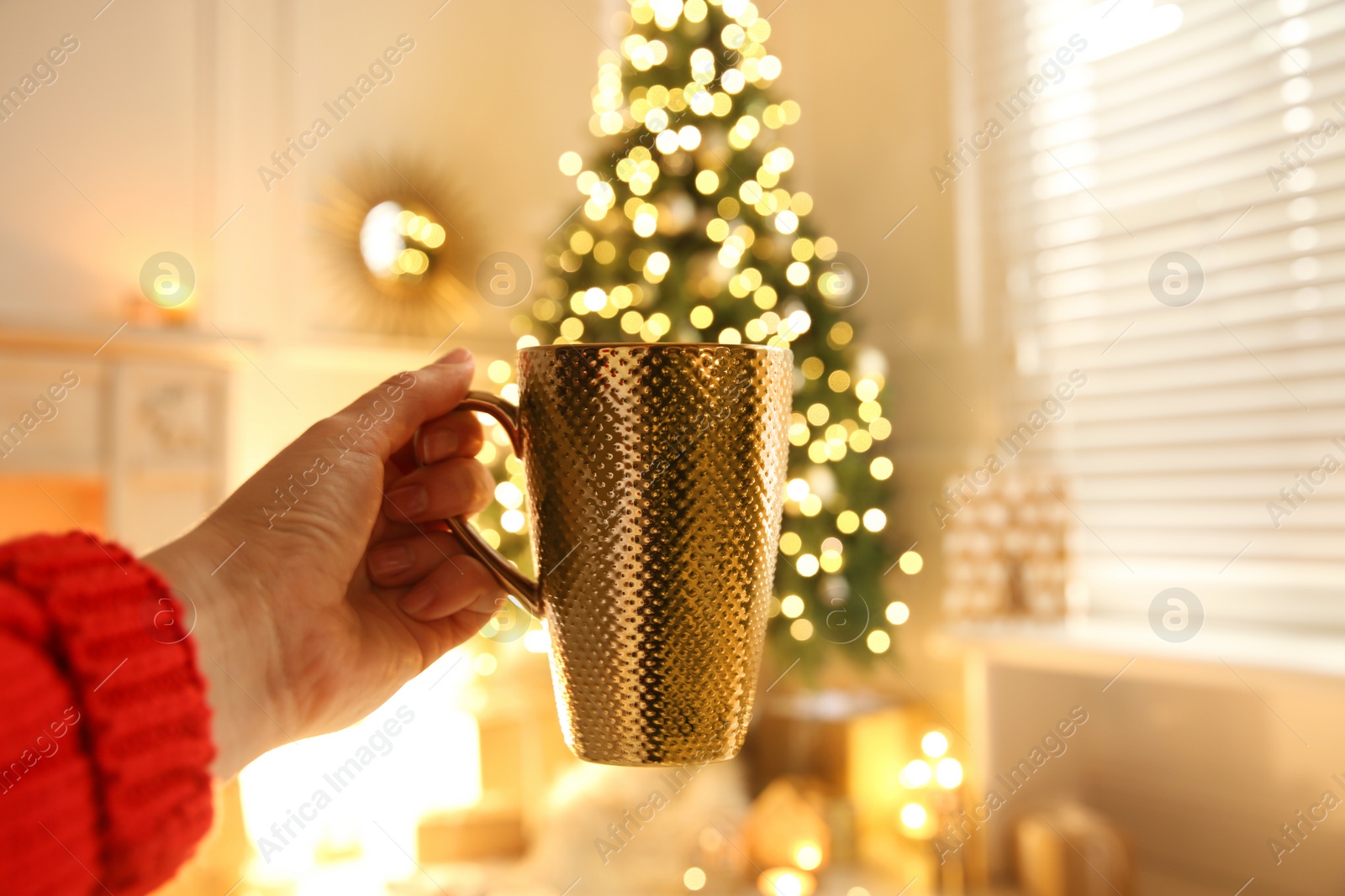 Photo of Woman with cup of drink and blurred Christmas tree on background, closeup