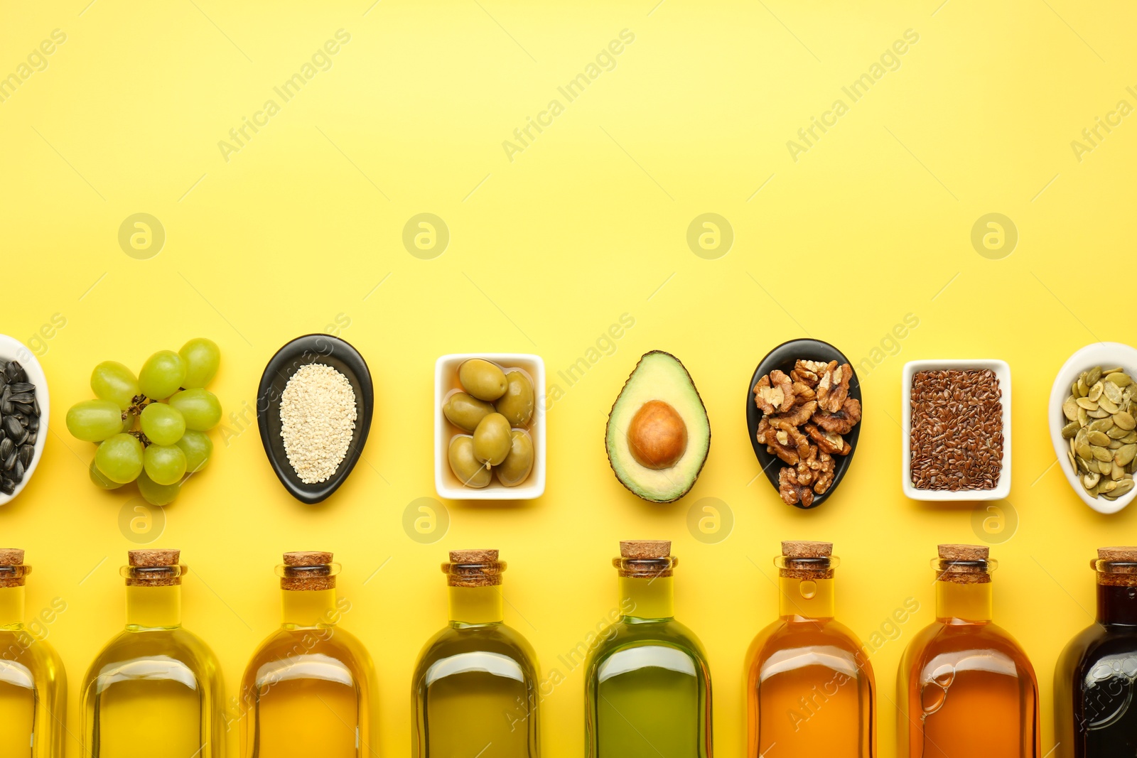 Photo of Vegetable fats. Different oils in glass bottles and ingredients on yellow table, flat lay. Space for text