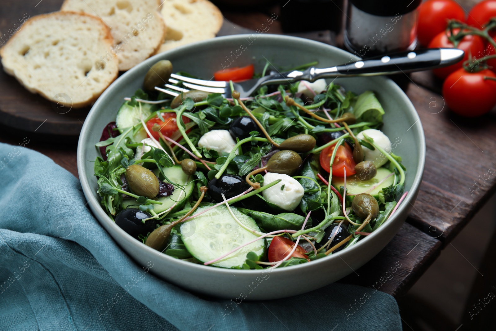 Photo of Fresh salad with vegetables, capers and mozzarella in bowl on wooden table, closeup