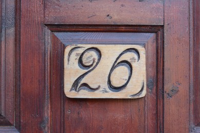 Photo of Plate with house number twenty six on wooden door, closeup