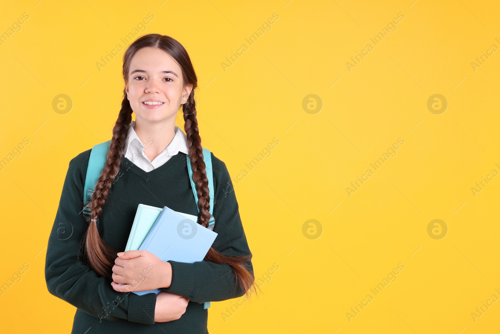 Photo of Teenage girl in school uniform with books and backpack on yellow background. Space for text