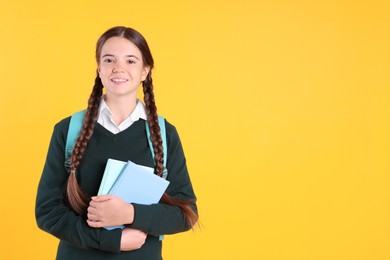 Teenage girl in school uniform with books and backpack on yellow background. Space for text