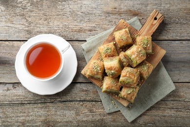 Delicious fresh baklava with chopped nuts and tea on wooden table, flat lay. Eastern sweets