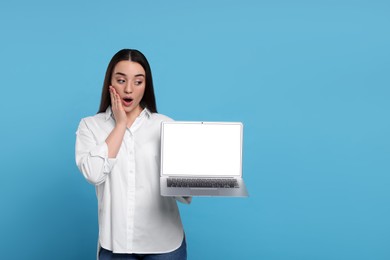 Surprised young woman showing laptop on light blue background, space for text