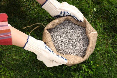 Woman with bag of fertilizer on green grass outdoors, top view