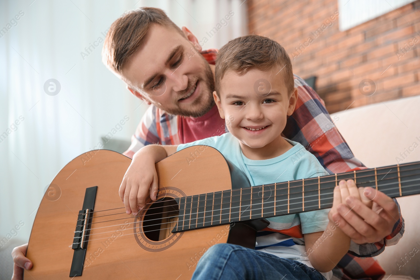 Photo of Father teaching his little son to play guitar at home