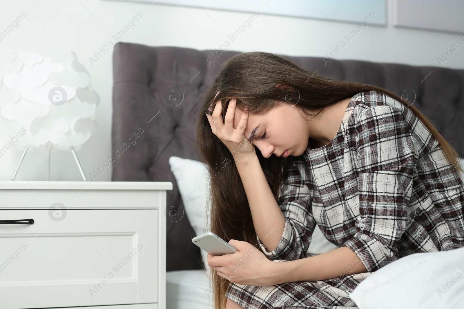 Photo of Upset teenage girl with smartphone sitting on bed. Space for text