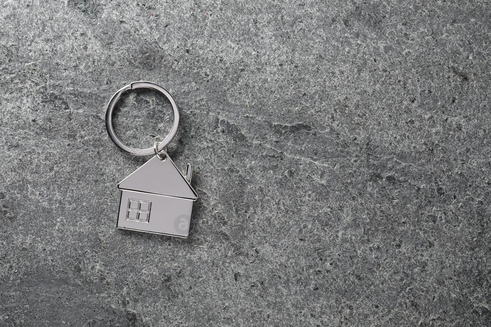 Photo of Metal keychain in shape of house on grey textured table, top view. Space for text