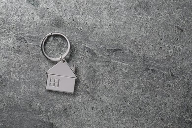 Photo of Metal keychain in shape of house on grey textured table, top view. Space for text