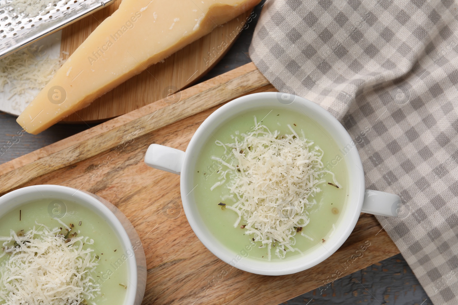 Photo of Delicious cream soup with parmesan cheese in bowls on grey wooden table, flat lay