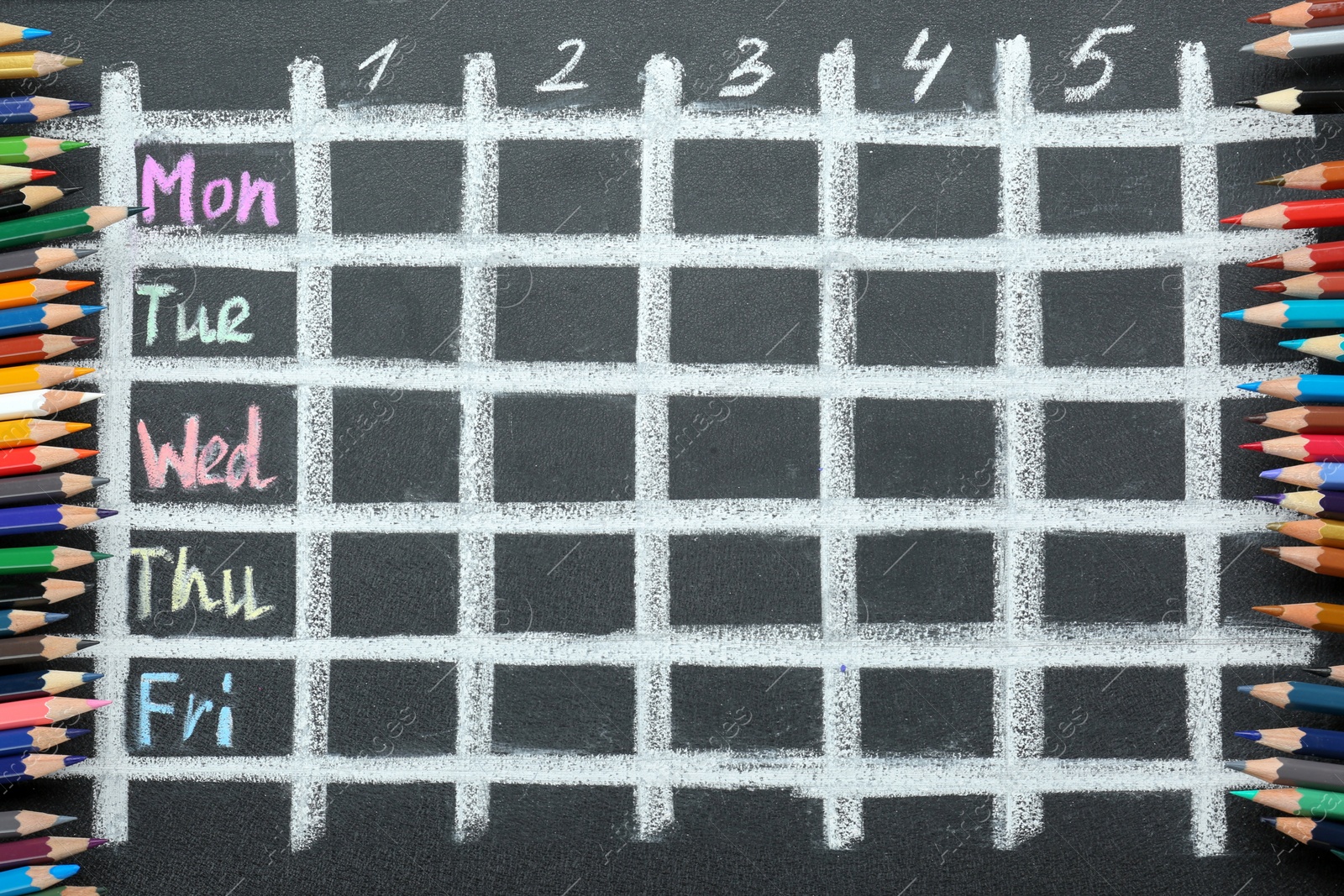 Photo of Colorful pencils and drawn weekly school timetable on black chalkboard, top view