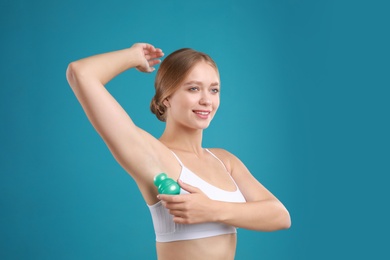 Young woman applying deodorant to armpit on teal background