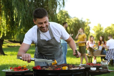 Photo of Man cooking meat and vegetables on barbecue grill in park