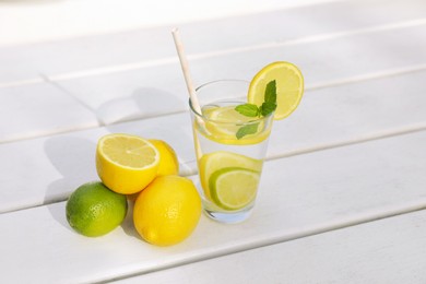 Photo of Glass of water with lemons, limes and mint on white wooden table outdoors