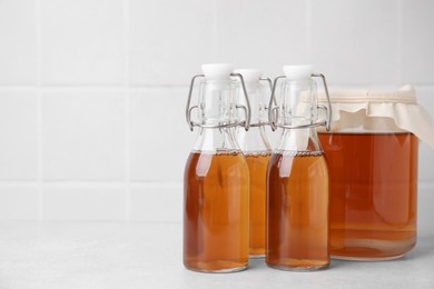 Tasty kombucha in glass jar and bottles on white table, space for text