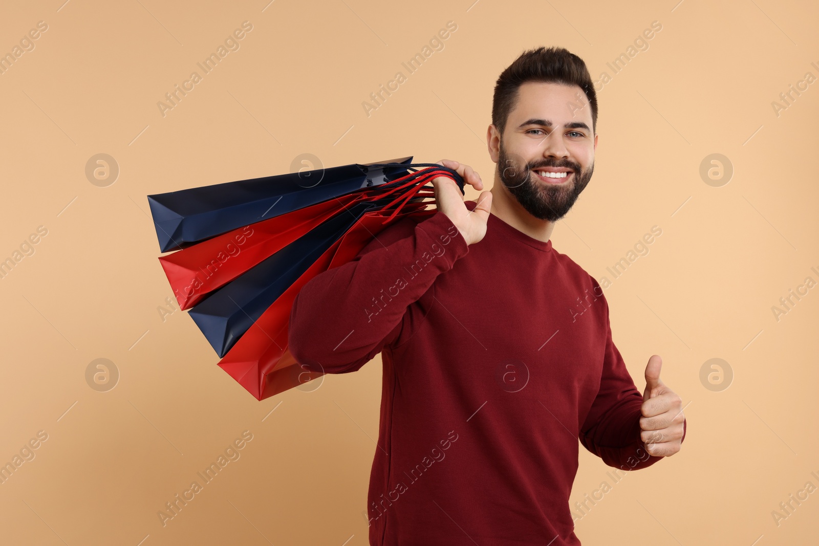 Photo of Smiling man with many paper shopping bags showing thumb up on beige background