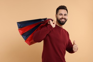 Smiling man with many paper shopping bags showing thumb up on beige background