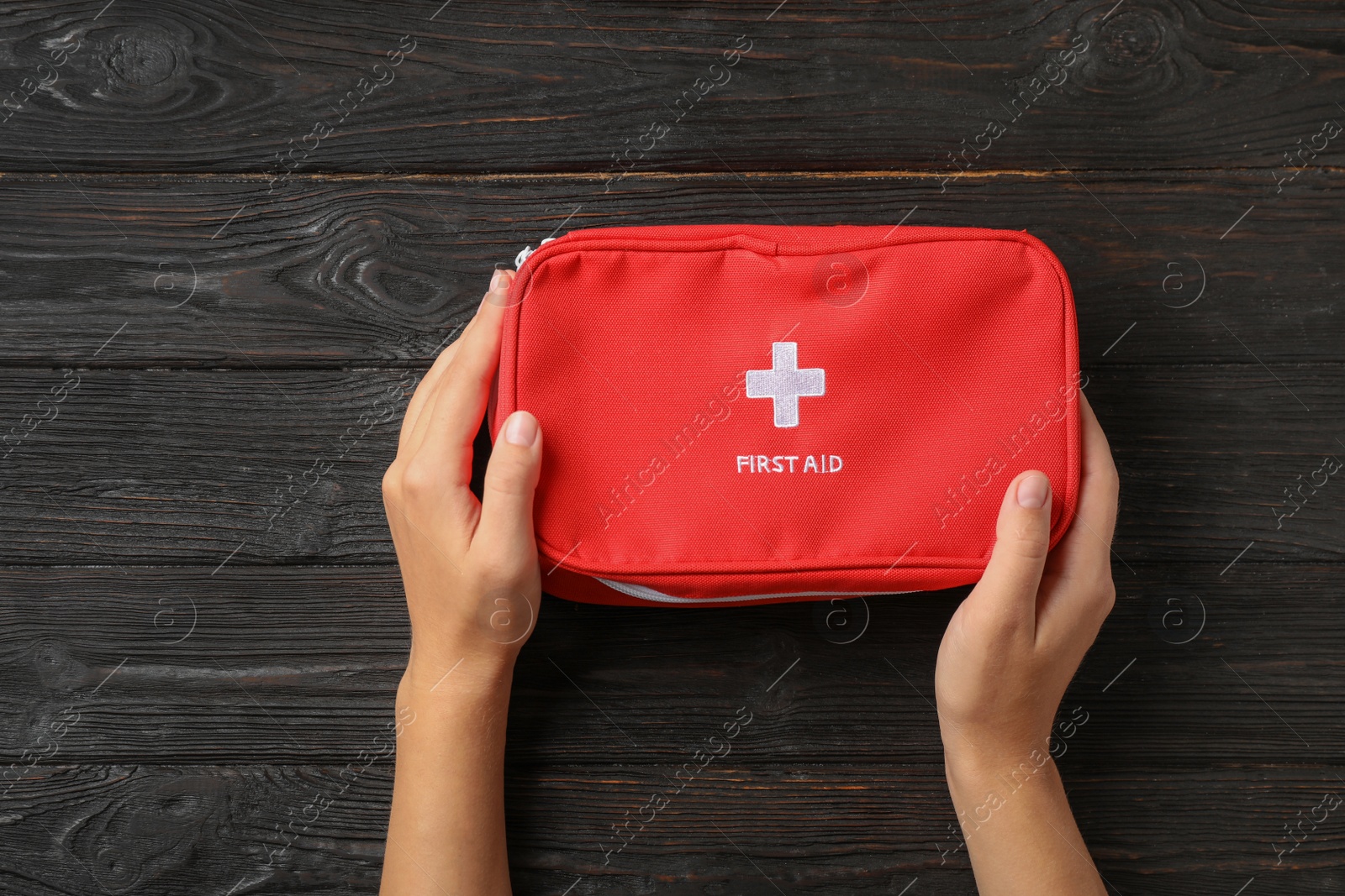 Photo of Woman holding first aid kit on dark table, top view