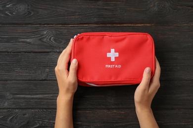 Photo of Woman holding first aid kit on dark table, top view