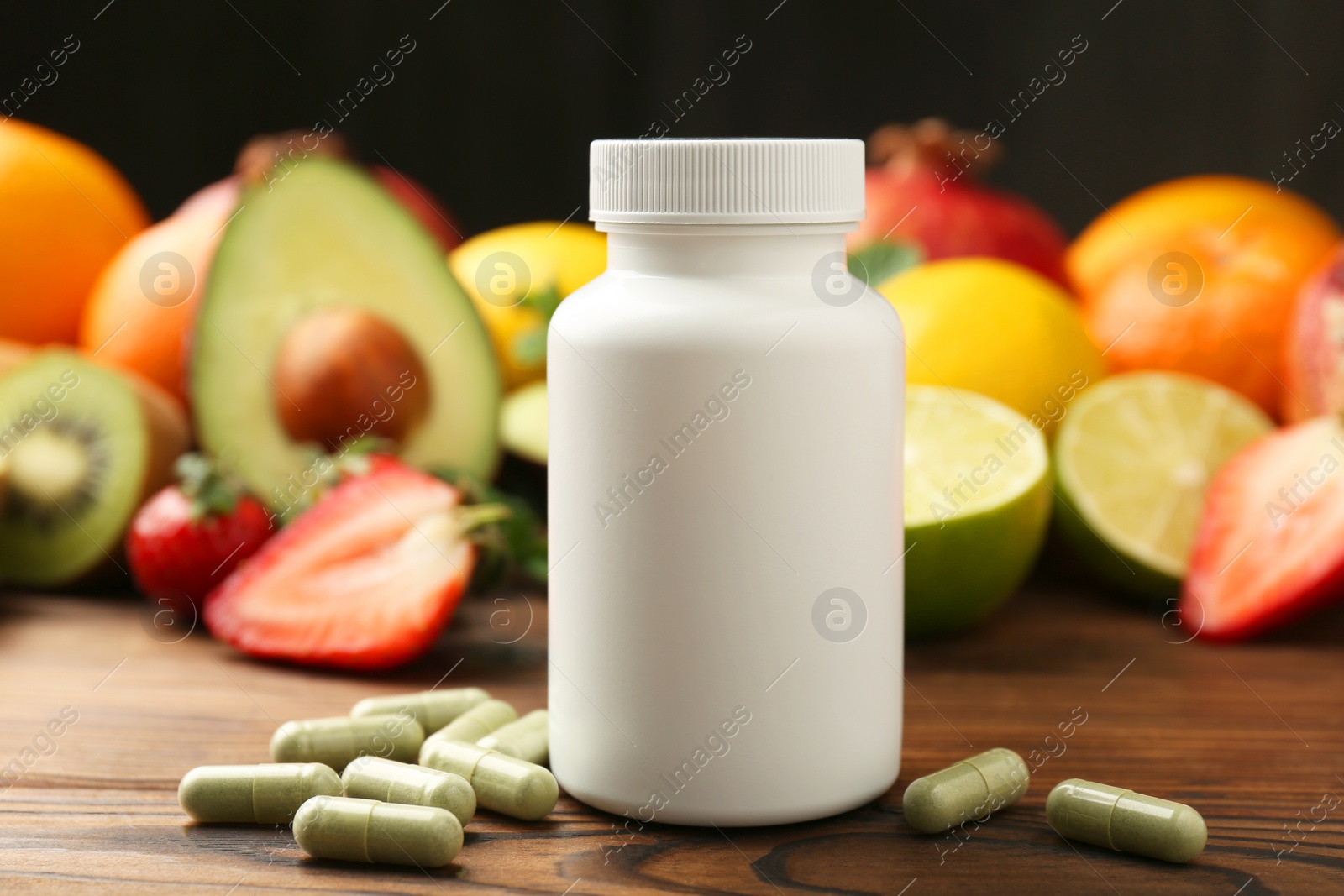 Photo of Vitamin pills, bottle and fresh fruits on wooden table, closeup