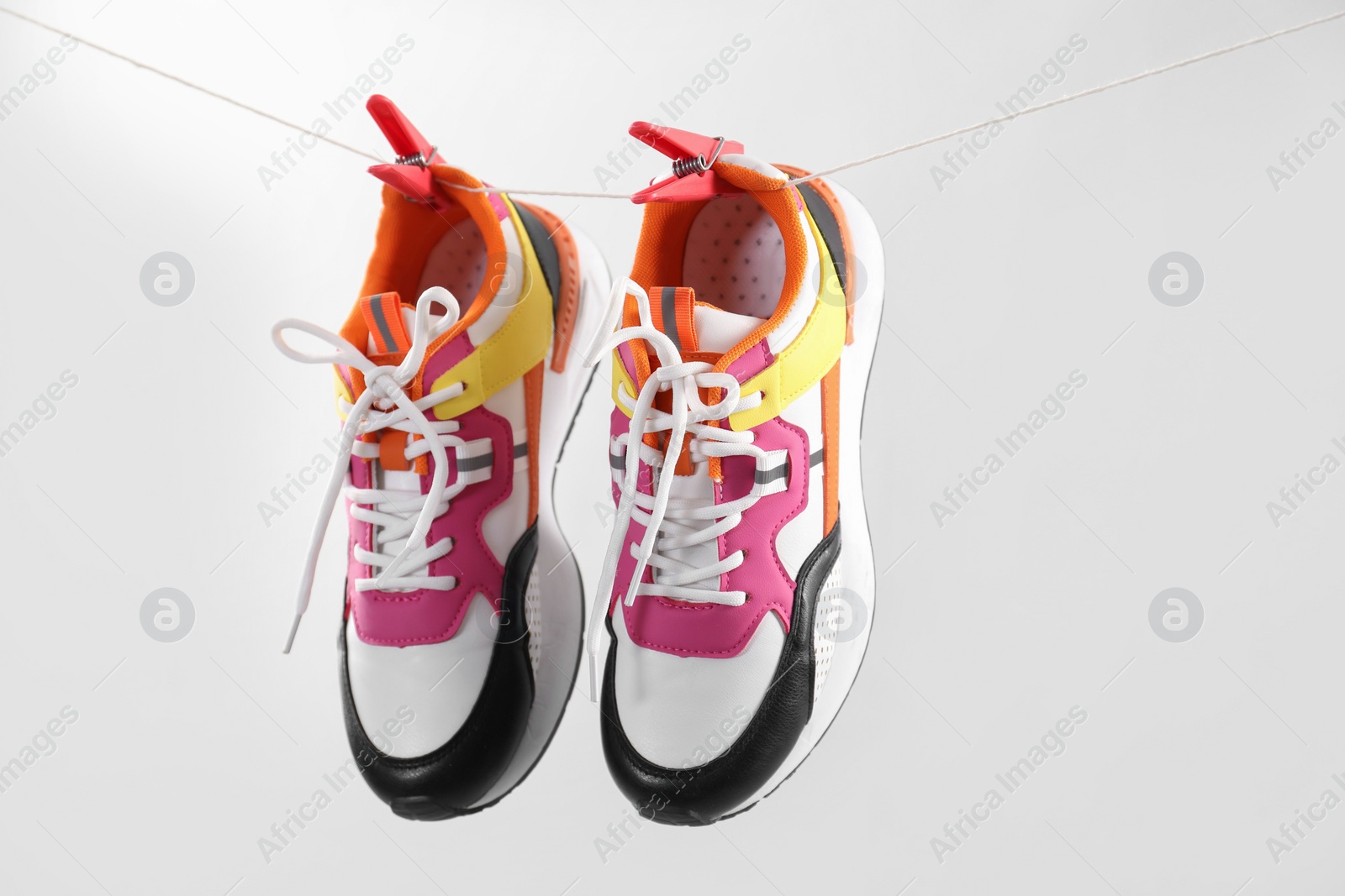 Photo of Stylish sneakers drying on washing line against light grey background