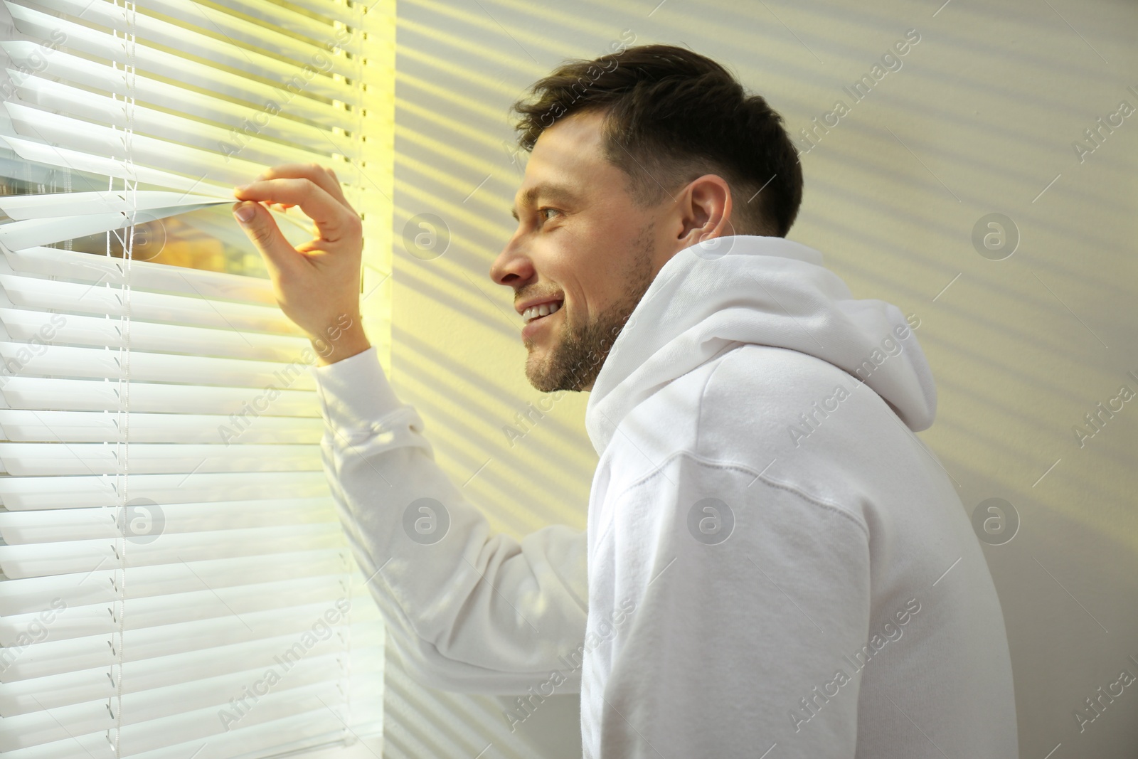 Photo of Handsome man opening window blinds at home
