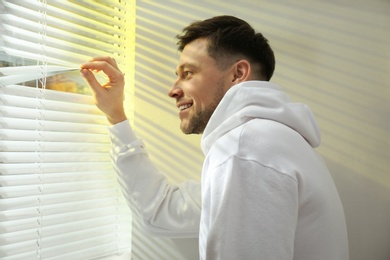 Handsome man opening window blinds at home