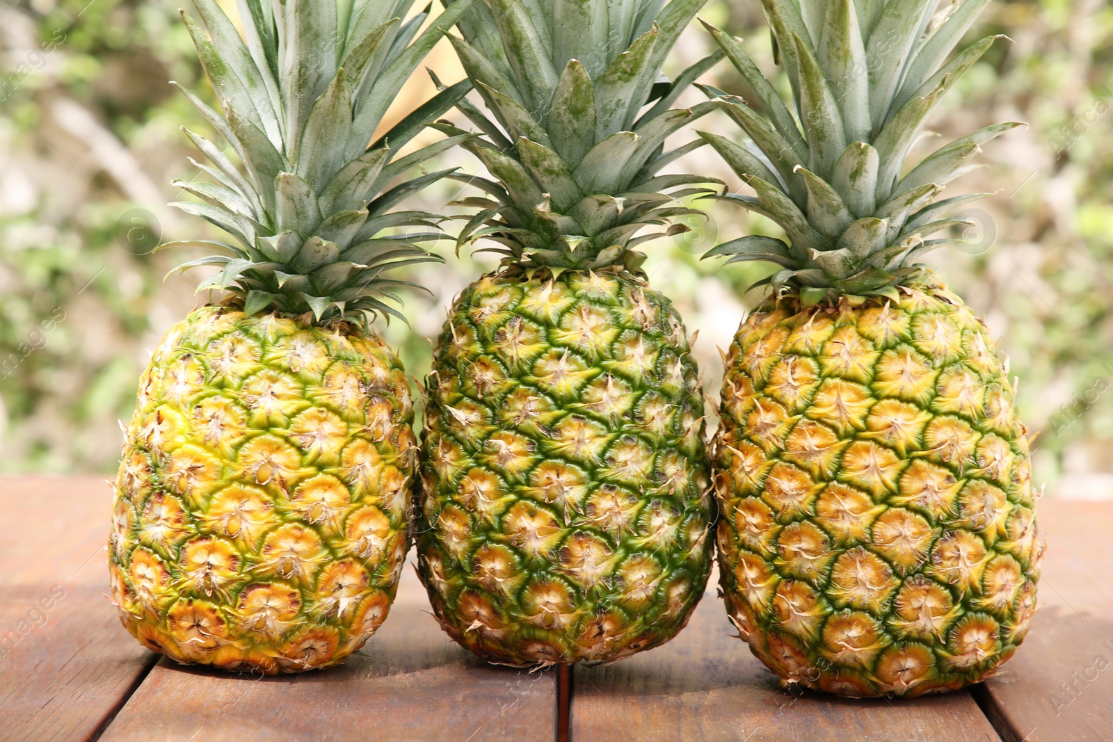 Photo of Delicious ripe pineapples on wooden table outdoors, closeup