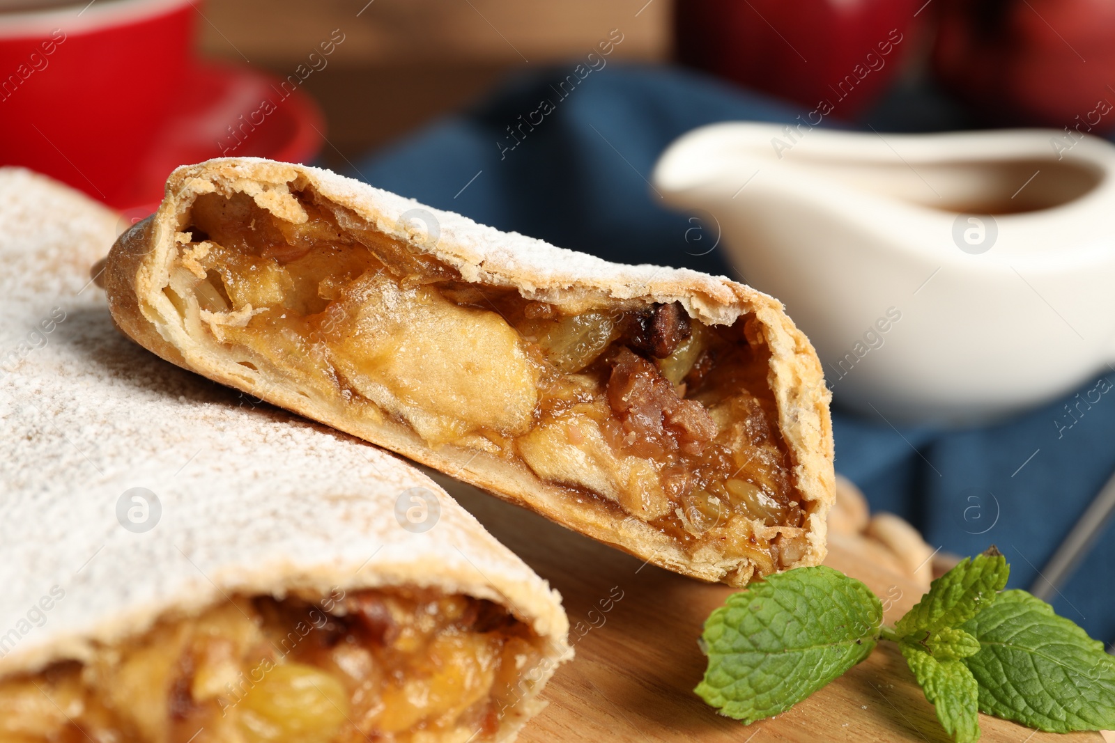 Photo of Delicious strudel with apples, nuts and raisins on wooden board, closeup