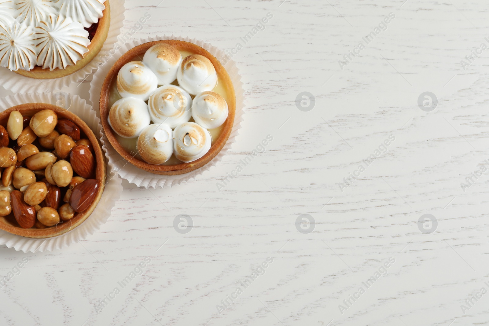 Photo of Different tartlets on white wooden table, flat lay with space for text. Tasty dessert