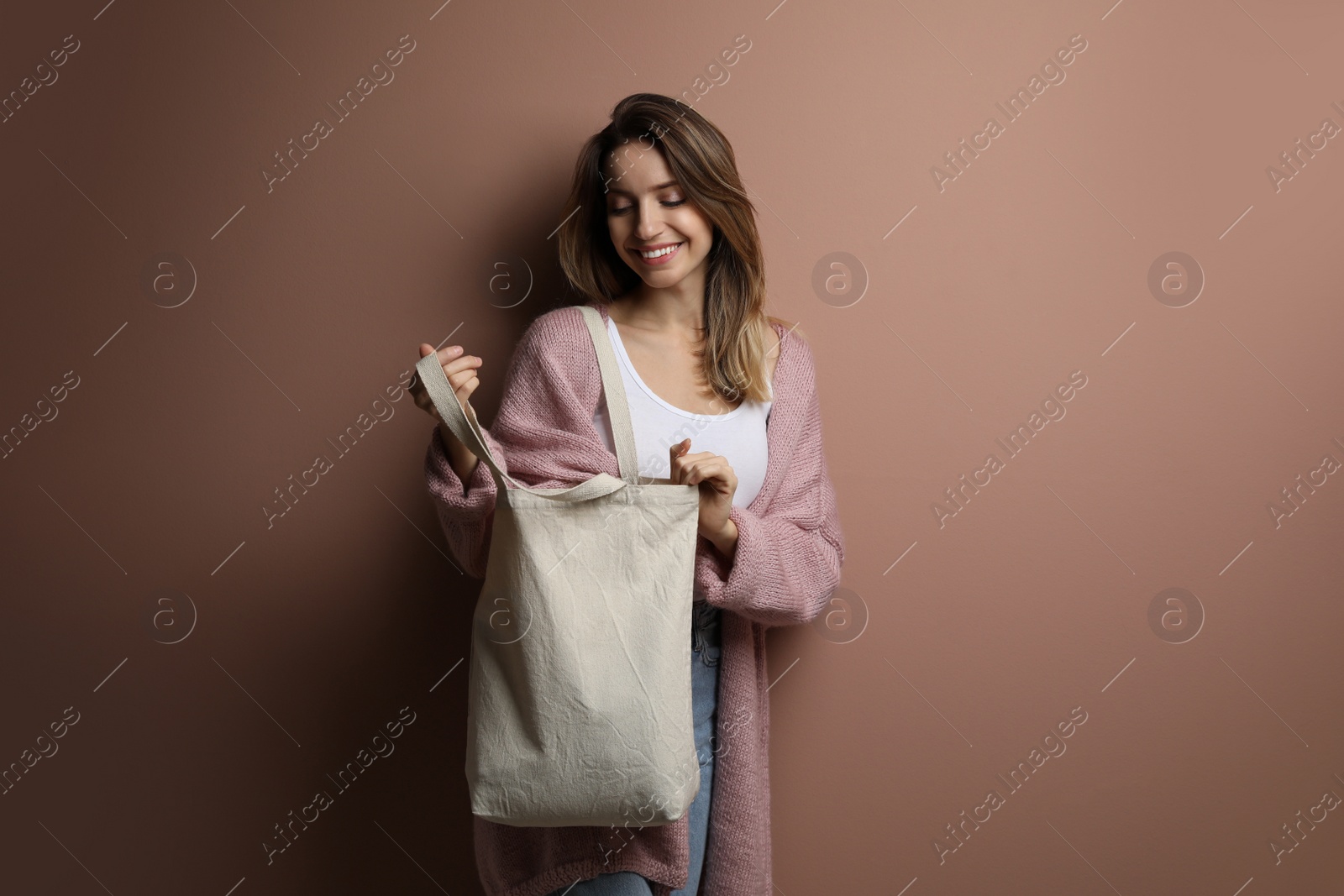 Photo of Happy young woman with blank eco friendly bag against light brown background